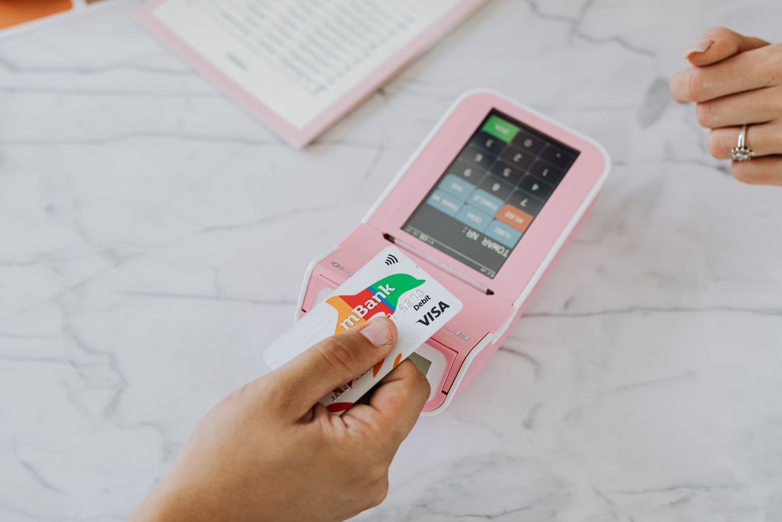 Une main approche une carte bancaire d'un terminal de paiement rose