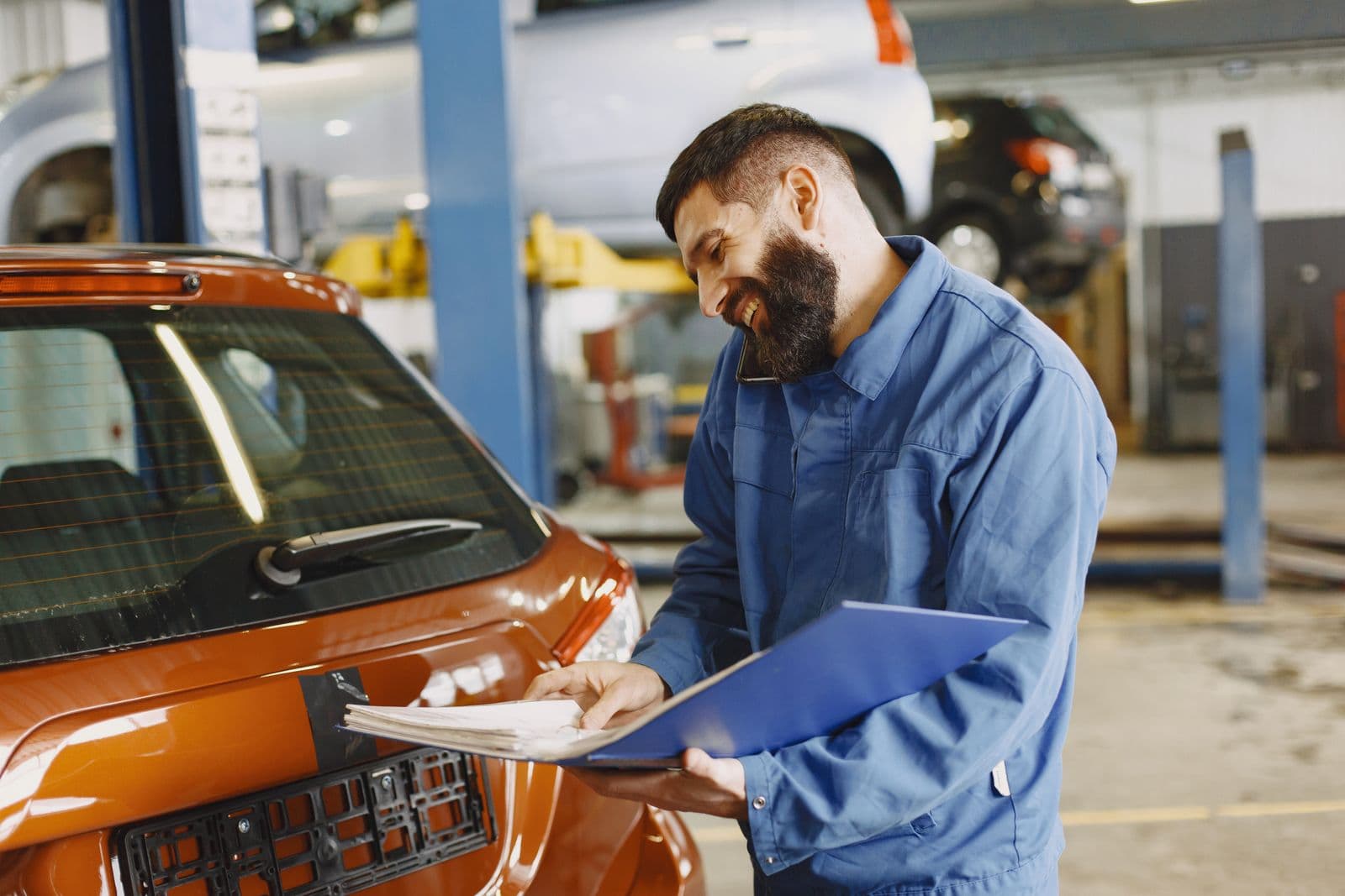Un contrôleur souriant, dossier à la main, examine une voiture orange dans son atelier