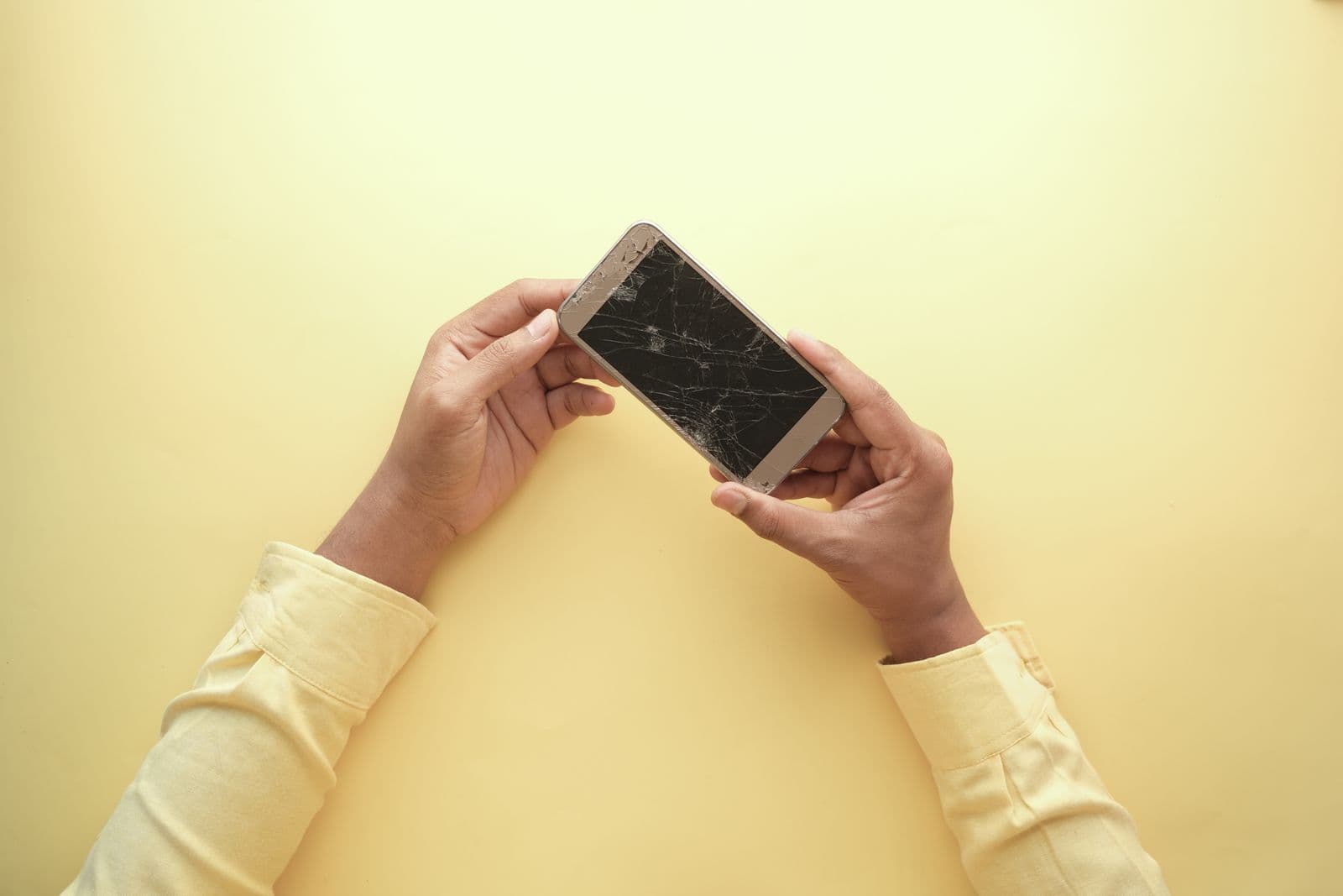 Mains tenant un smartphone à l'écran fissuré, illustrant la question de l'assurance des appareils mobiles
